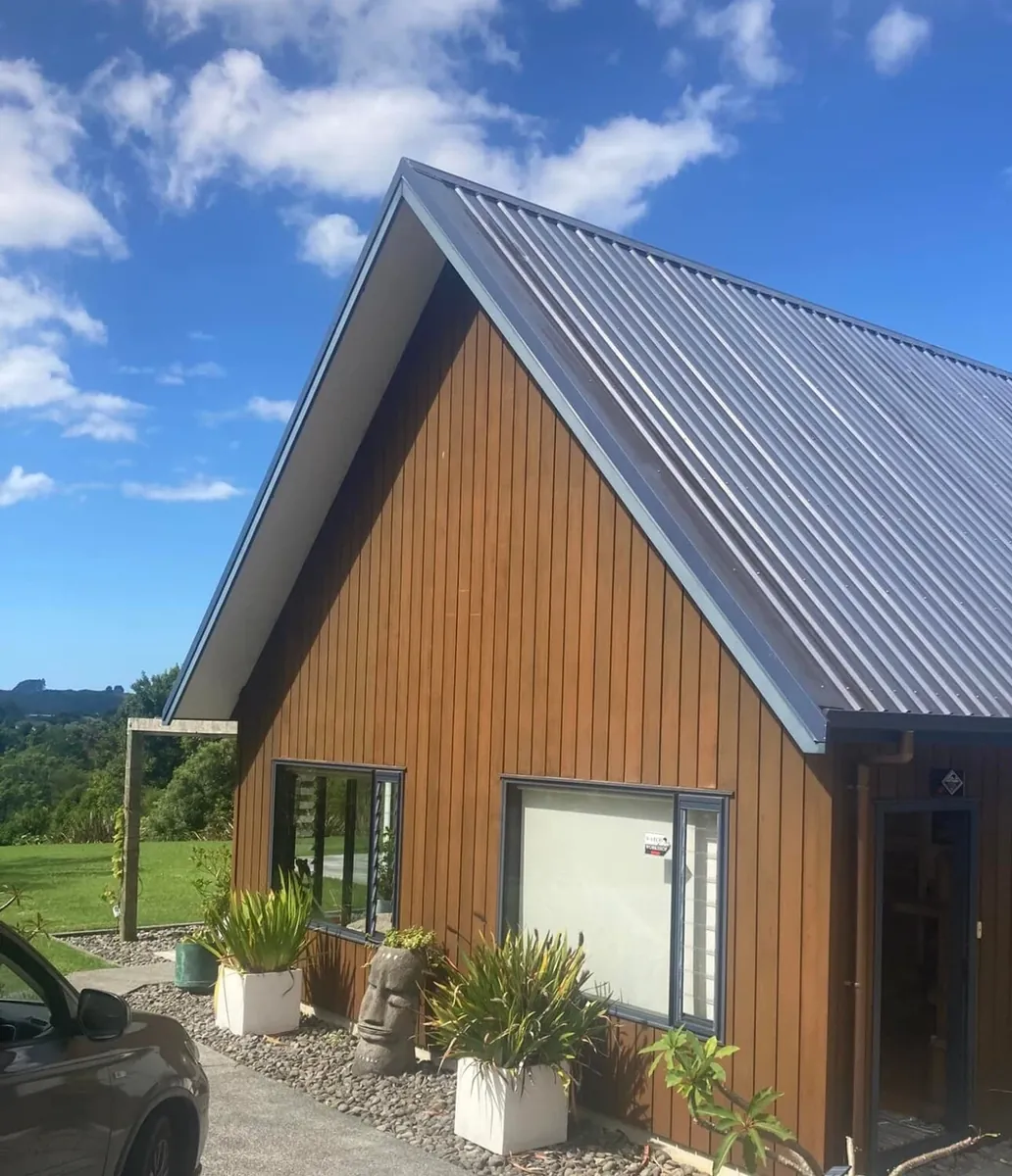 Before: a gabled house with brown stained timber cladding