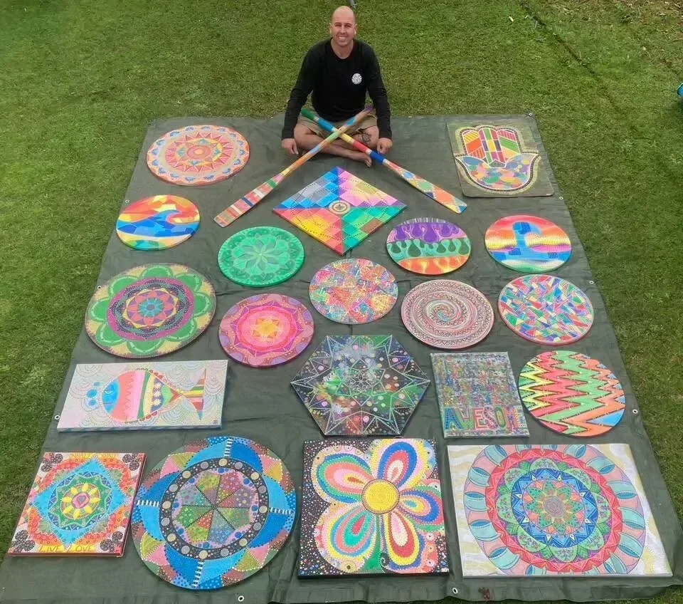 Jef sitting on the grass behind a spread of his colourful hand-painted artworks