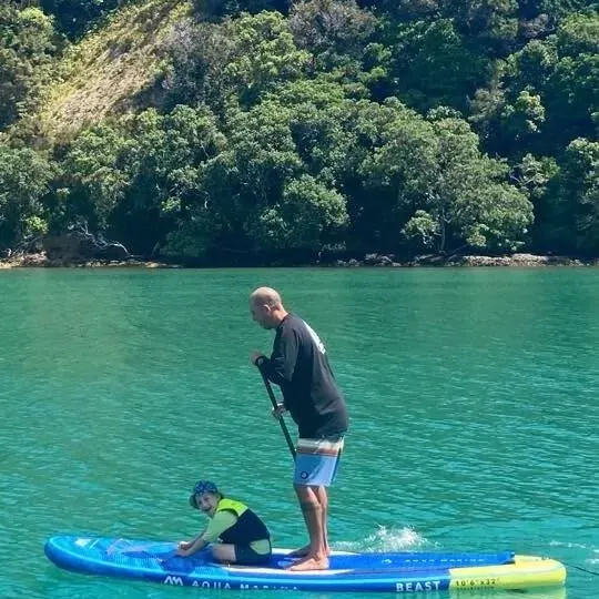 Stand-up paddleboarding on clear green water with a child sitting on the board